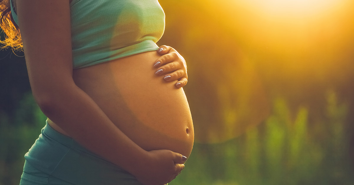 Adult pregnant woman on against the backdrop of the sunset in th